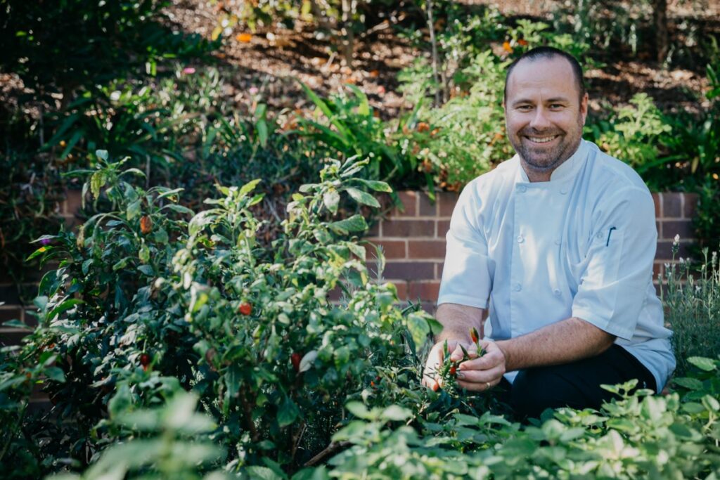 Chef smiling in a lush garden at The Botanica Vaucluse.