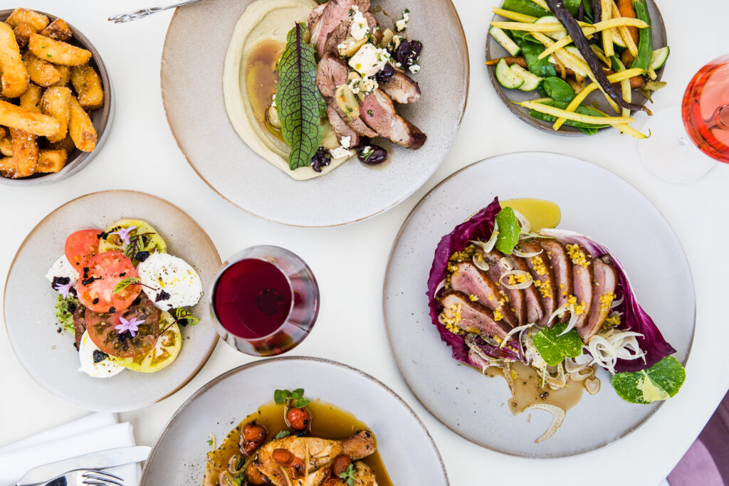 A variety of gourmet farm-to-table dishes and wine glasses laid out on a table at The Botanica Vaucluse.
