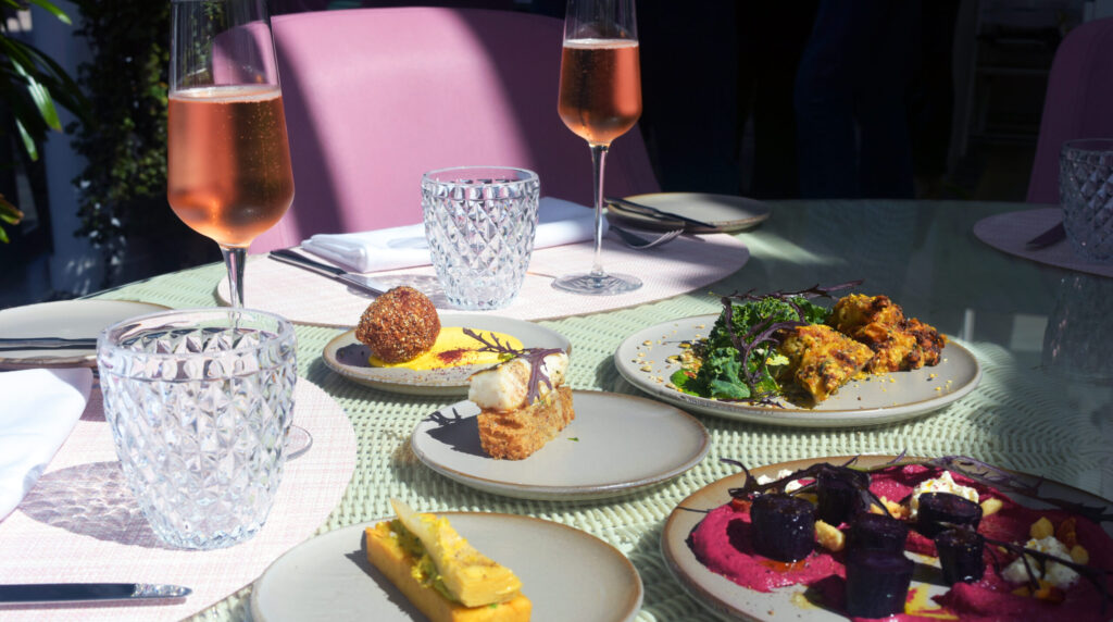Sunlit table setting featuring colorful gourmet dishes and glasses of sparkling wine at The Botanica Vaucluse.