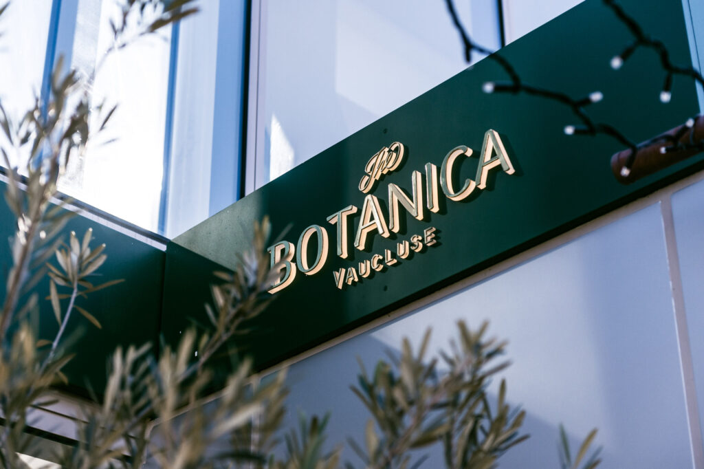 The outdoor entrance sign for The Botanica Vaucluse restaurant in gold lettering on a green background.
